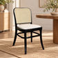 A dining chair with a black wooden frame, woven cane backrest, and a light beige upholstered seat cushion, shown in a bright, modern dining room setting.