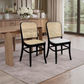 Two dining chairs with black frames and woven cane backs, one with a light wood seat and one with a white seat, placed in a bright dining room next to a wooden table.