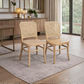 Two light natural wood dining chairs with woven cane backs, placed on a gray rug in a bright, modern dining room.