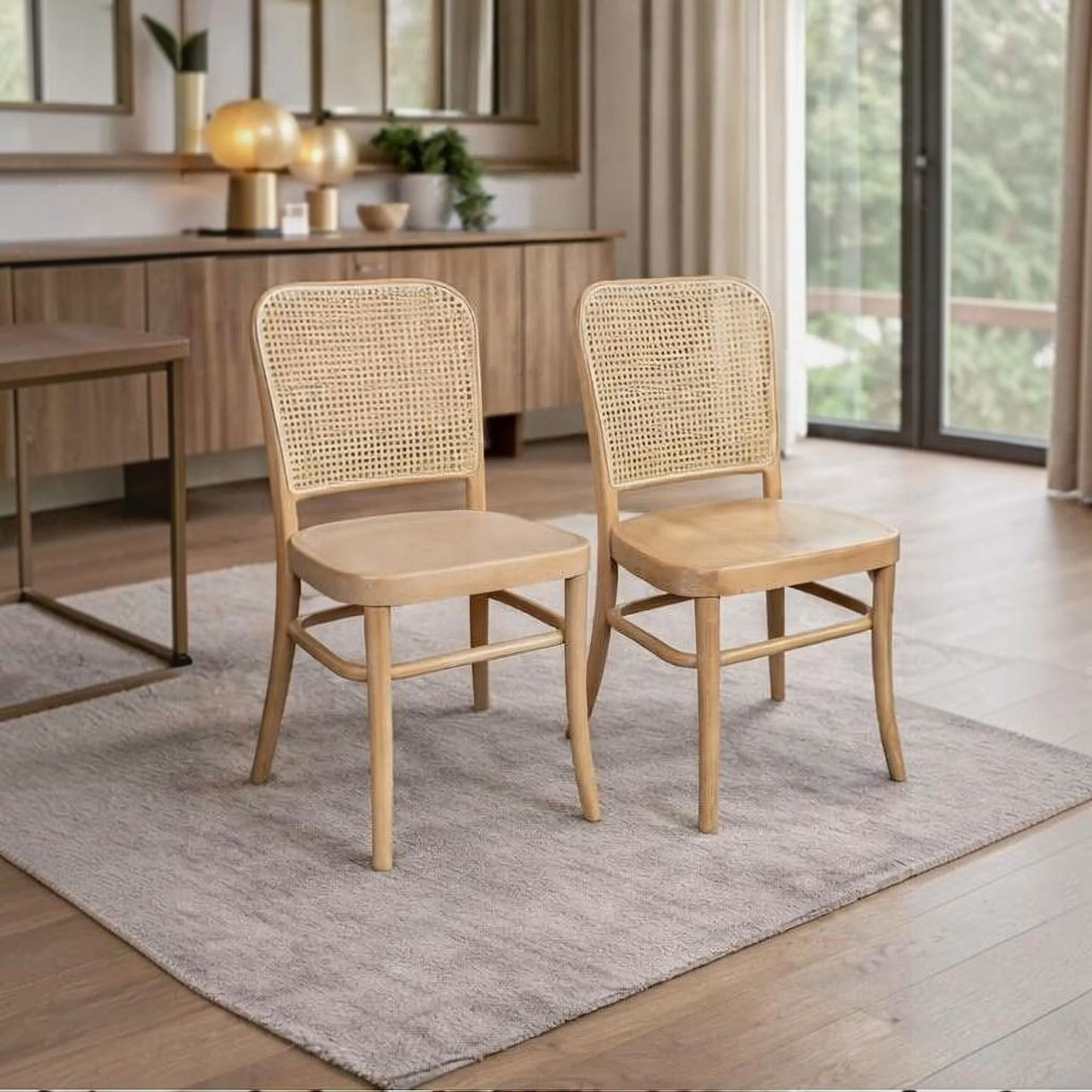 Two light natural wood dining chairs with woven cane backs, placed on a gray rug in a bright, modern dining room.