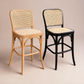 Two bentwood bar stools with woven cane seats and backs, shown side by side on a warm beige studio background. One stool has a light natural wood frame, and the other has a black frame.