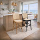 Two bar stools in a bright, modern kitchen with an ocean view. One stool has a light natural wood frame and woven cane seat, and the other has a black metal frame with a woven cane seat.