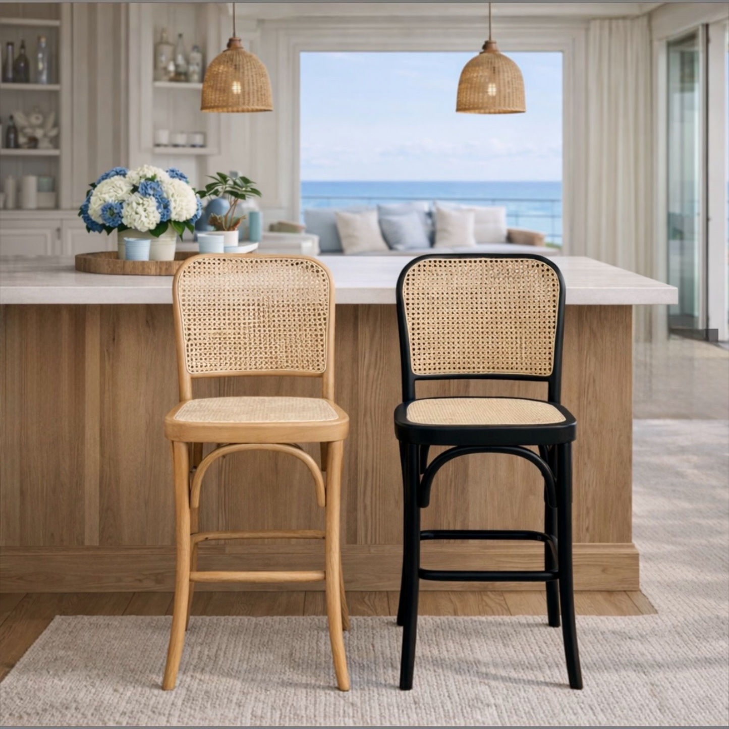 Two bar stools with woven cane backs and seats are shown in a bright, modern kitchen setting. The left stool has a light natural wood frame, and the right stool has a black metal frame with a beige woven cane back and seat.