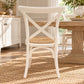 A white wooden dining chair with a woven cane seat, positioned in a bright, sunlit dining room next to a rustic wooden table on a jute rug.