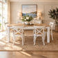 A white wooden dining table with six matching white chairs in a bright, modern dining room setting. The room features a large woven jute rug, wood floors, wall paneling, and a framed landscape painting above a console table.