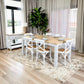 A dining room scene showing a rectangular table with a light natural wood top and white legs, surrounded by six white chairs with wooden seats. The table and chairs are placed on a large beige patterned area rug in a bright room with wood floors, sheer curtains, and a potted plant in the background.