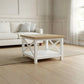A white wooden coffee table with a light natural wood top and a lower shelf, styled in a bright, modern living room with a white sofa and light wood floors.