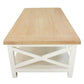 A rectangular coffee table with a light natural wood top and a white painted frame featuring an X-shaped support design on the front and a lower shelf.