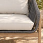 Close-up of an outdoor sofa cushion set with a light beige fabric seat cushion, back cushion, and dark gray woven rope armrests on a light wood frame.