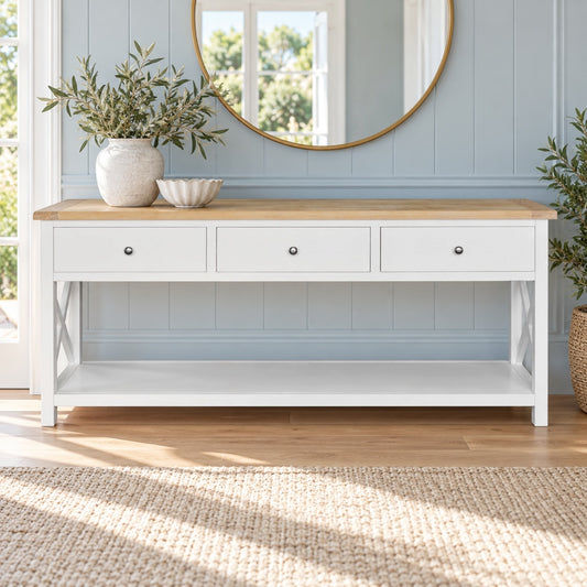 A white console table with a light wood top, three drawers, and an open lower shelf, styled in a bright entryway with a mirror, plants, and a woven rug.