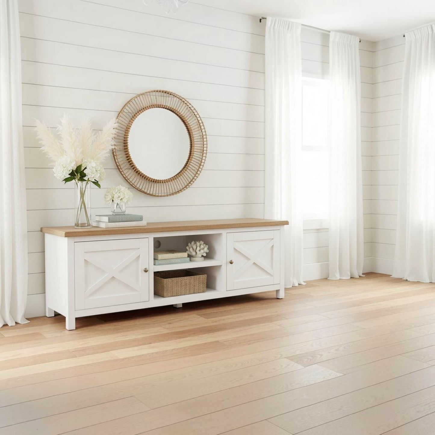 A white wooden media console with a light wood top, styled in a bright, modern farmhouse room with white shiplap walls, sheer curtains, and light oak flooring.