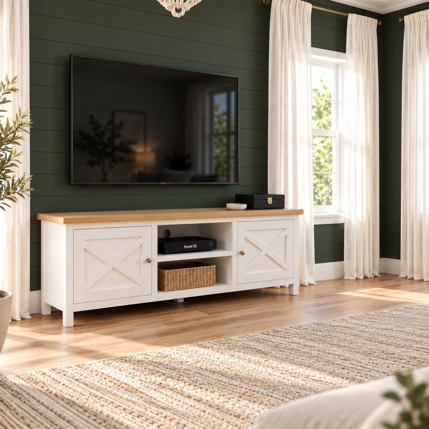 A white wooden TV stand with a light oak top and brass hardware, styled in a living room against a dark green shiplap wall with a mounted television.