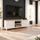 A white TV stand with a light wood top and brass hardware, styled in a modern living room setting against a dark gray shiplap wall with a flat-screen TV mounted above.