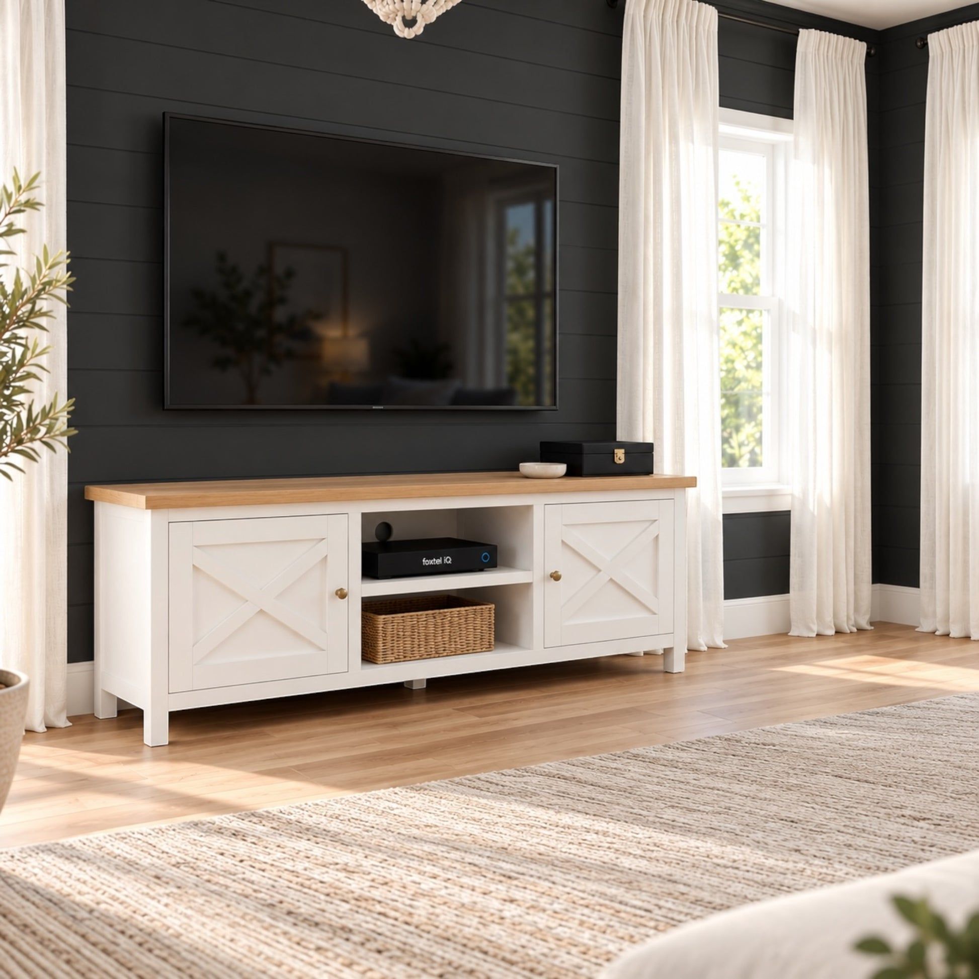 A white TV stand with a light wood top and brass hardware, styled in a modern living room setting against a dark gray shiplap wall with a flat-screen TV mounted above.