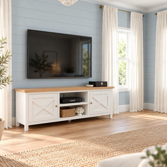 A white TV stand with a light wood top and brass hardware, styled in a bright living room with a blue shiplap wall, white curtains, and a flat-screen TV mounted above it.