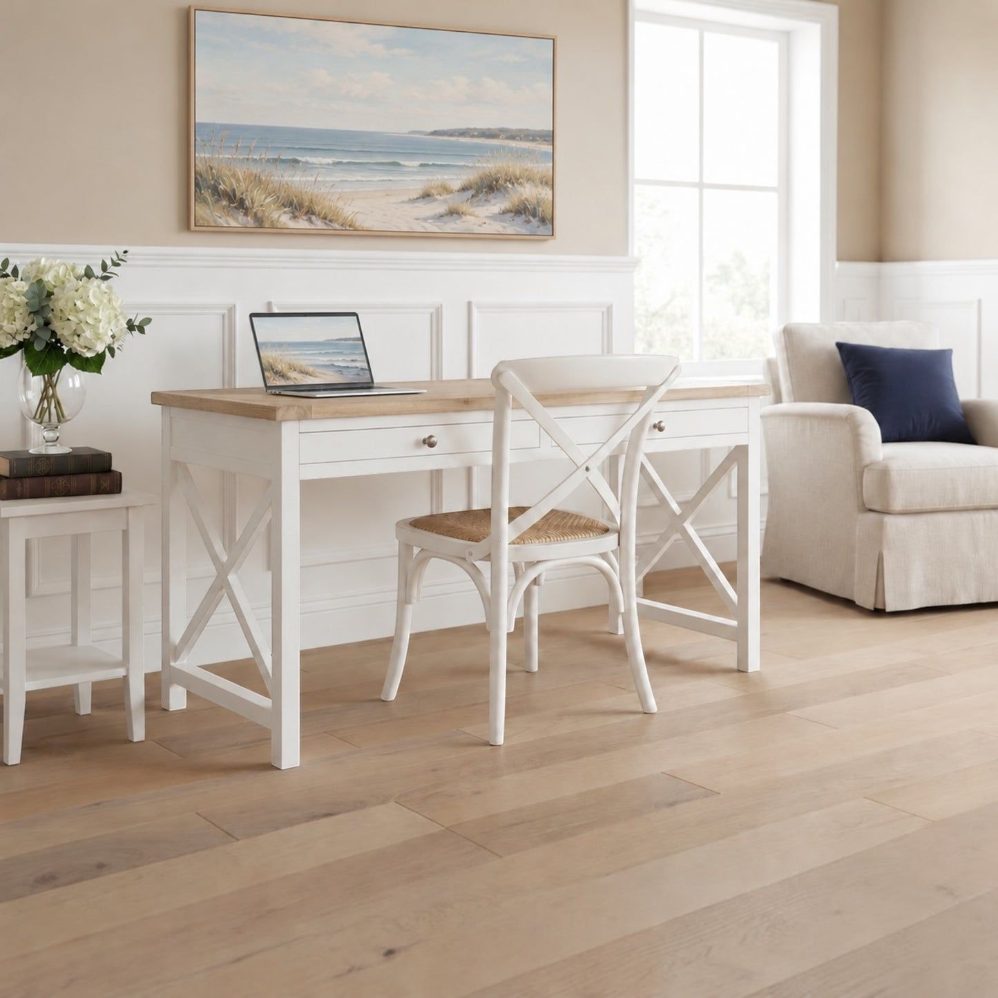 A white writing desk with a light wood top and matching white chair in a bright, neutral-toned home office setting with a beach painting on the wall.