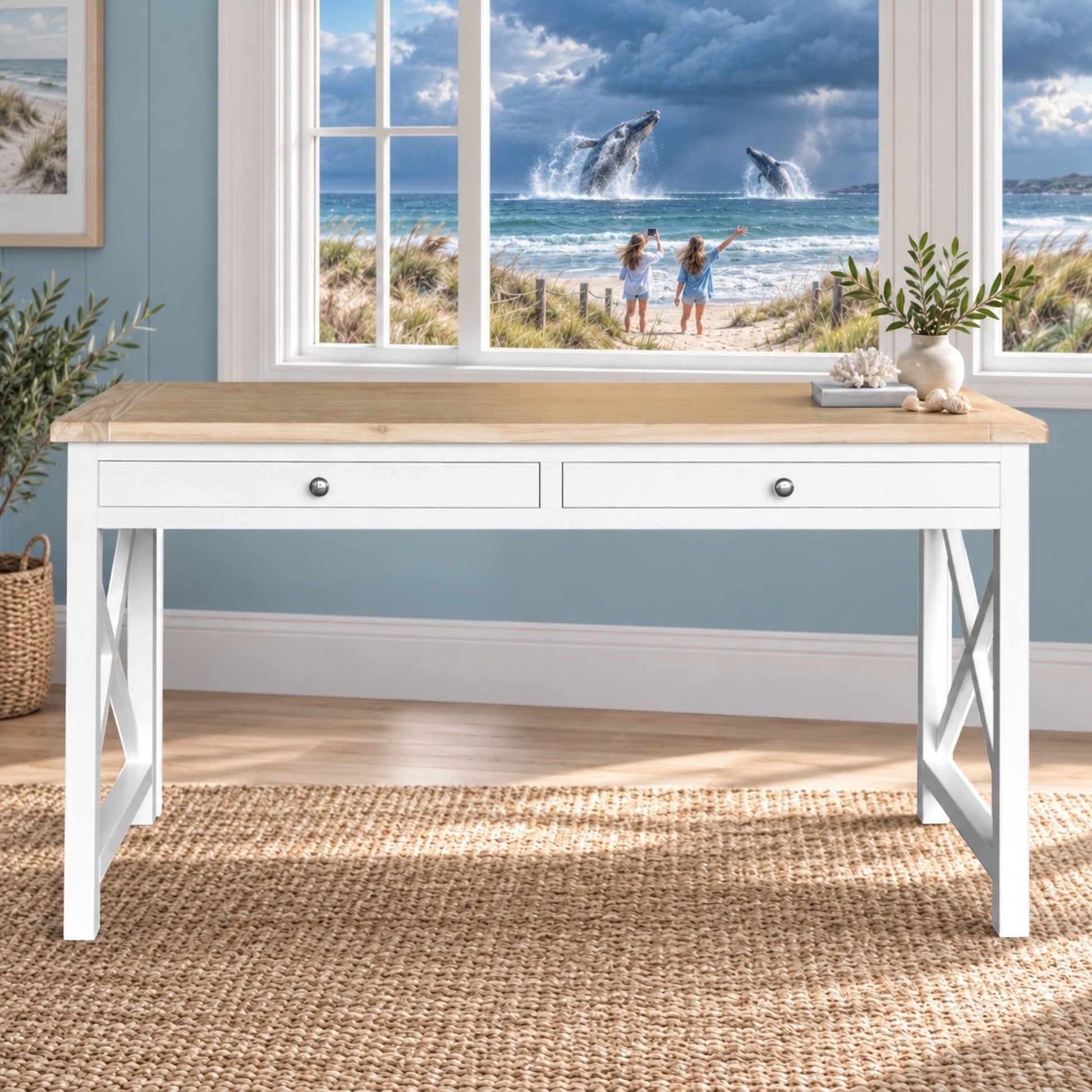 A white writing desk with a light wood top and two drawers, styled in a coastal-themed room with a window showing a beach scene with whales in the background.