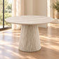 A round dining table with a textured, ribbed pedestal base in a light beige stone or concrete finish, set in a bright room with wooden floors and natural light.