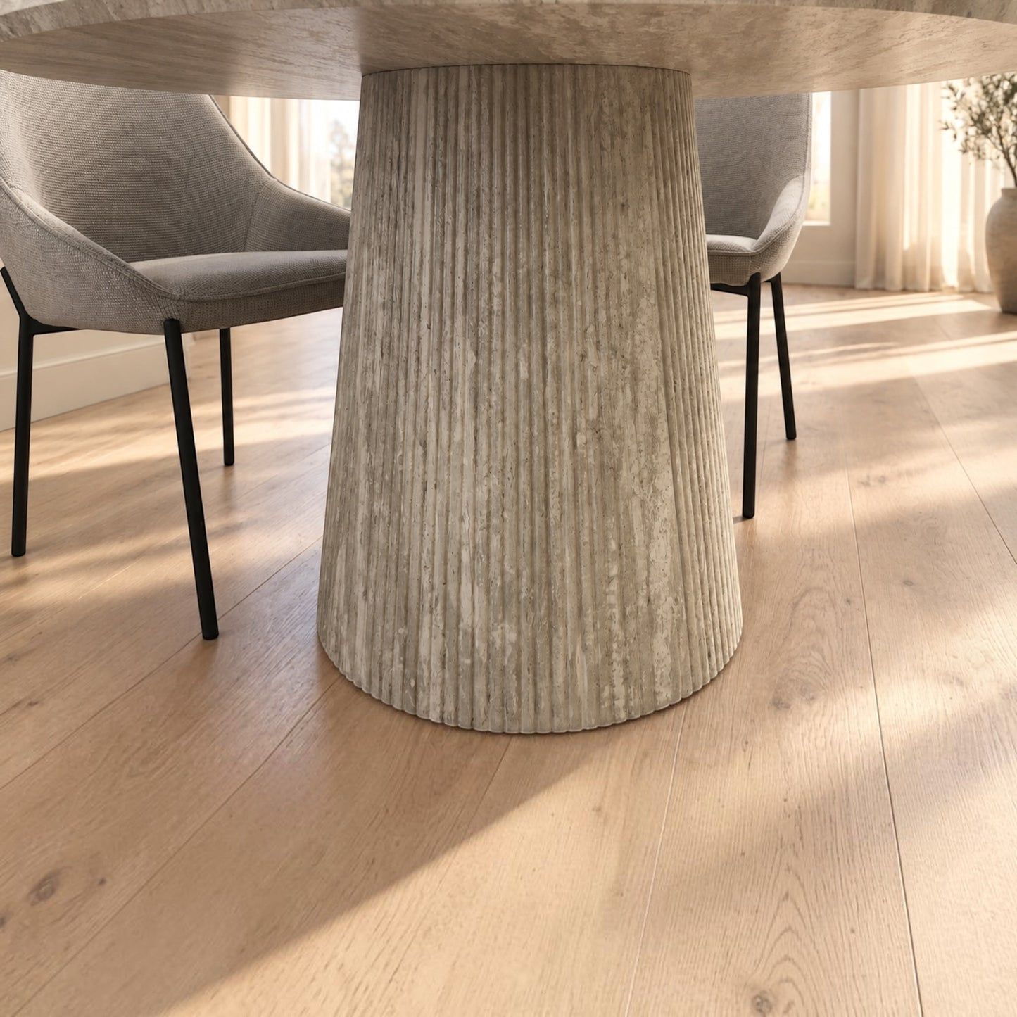 A close-up view of a light wood dining table with a fluted pedestal base, set in a bright room with light gray upholstered chairs and a light oak floor.