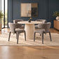 A round dining table with a ribbed pedestal base and four upholstered gray chairs, arranged on a light beige rug in a modern dining room with dark blue walls and wood flooring.