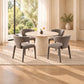 A modern dining set featuring a round ribbed pedestal table and four upholstered gray chairs, arranged on a light beige rug in a bright, sunlit room with large windows and a view of green trees.