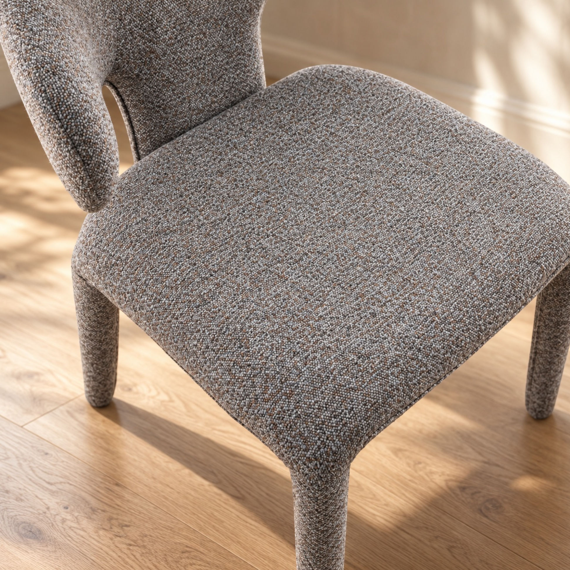 A close-up of a modern upholstered dining chair with a textured gray and beige bouclé fabric, set on a light wood floor.