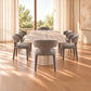 A modern dining set featuring a rectangular stone-look table and six upholstered chairs in a warm, sunlit room with wood floors and large windows.
