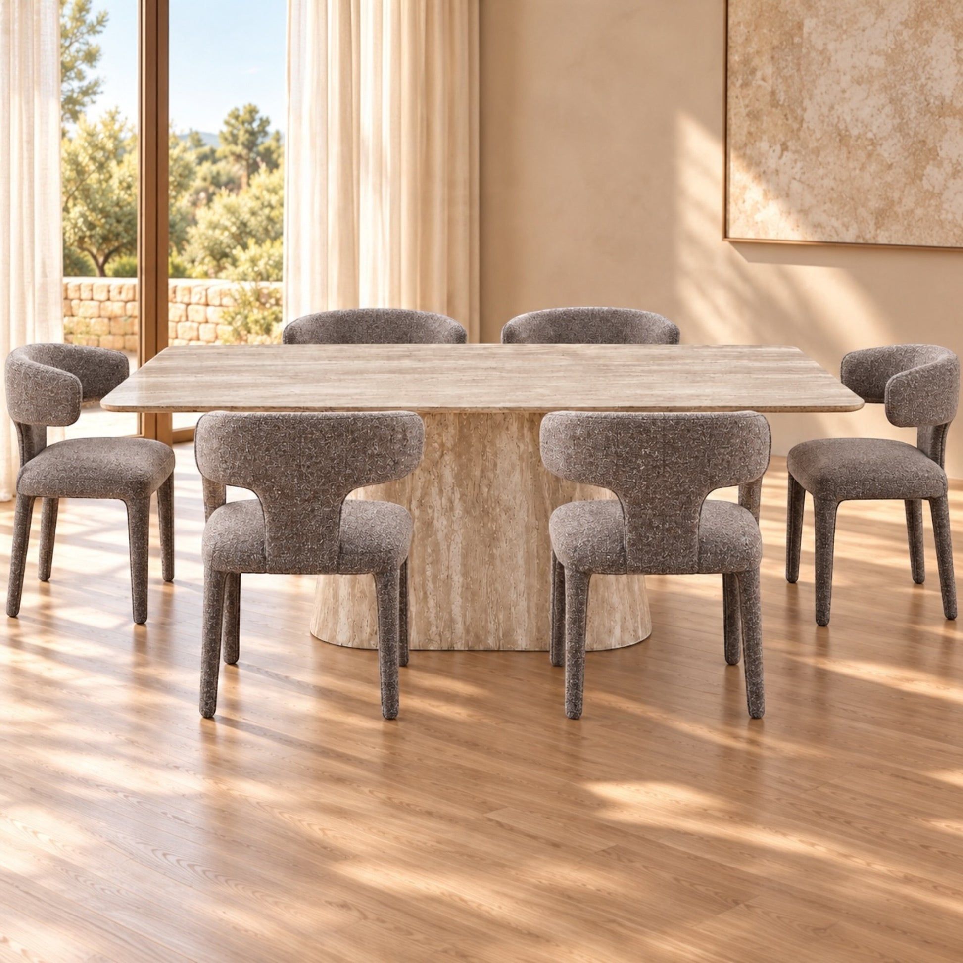 A modern dining set featuring a rectangular light stone table and six upholstered gray chairs, set in a bright room with warm wood floors and large windows.
