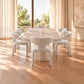 A modern dining set featuring a rectangular light wood table and six upholstered dining chairs in a warm, sunlit room with tall windows and curtains.