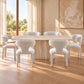 A modern dining set featuring a rectangular stone table and six upholstered chairs in a warm, sunlit room with beige walls and wood flooring.