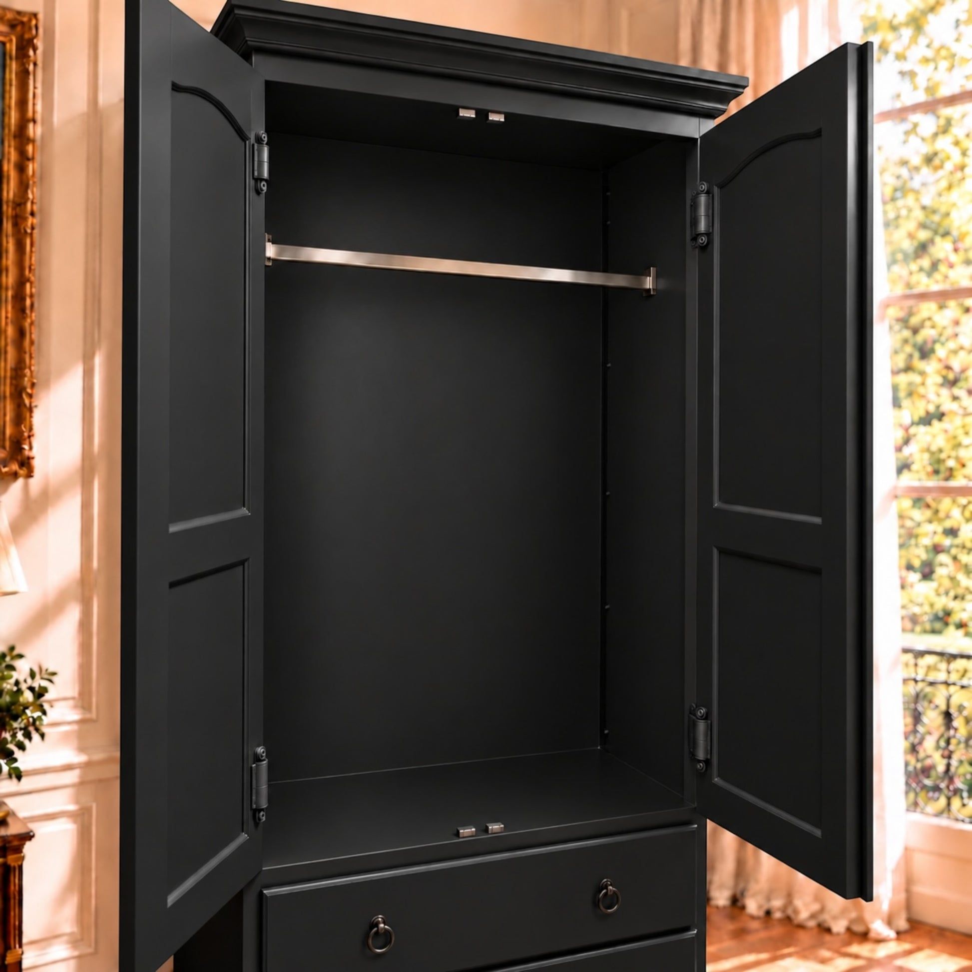 A tall black armoire or wardrobe cabinet with two open doors, a metal hanging rod, and a lower drawer, shown in a real interior room with warm sunlight and window light.