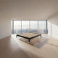 A minimalist black solid vic ash bed frame with light wood slats, positioned in a bright, modern bedroom with large floor-to-ceiling windows overlooking a city skyline.