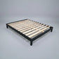 A modern platform solid vic ash frame with a matte black metal frame and natural wood slats, shown on a neutral gray studio background.
