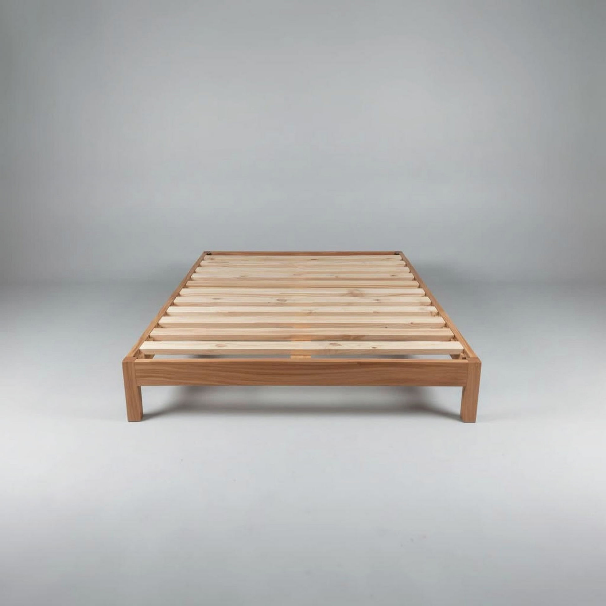 A minimalist wooden bed frame with a slatted platform base, shown from a front-three-quarters angle against a neutral gray studio background.