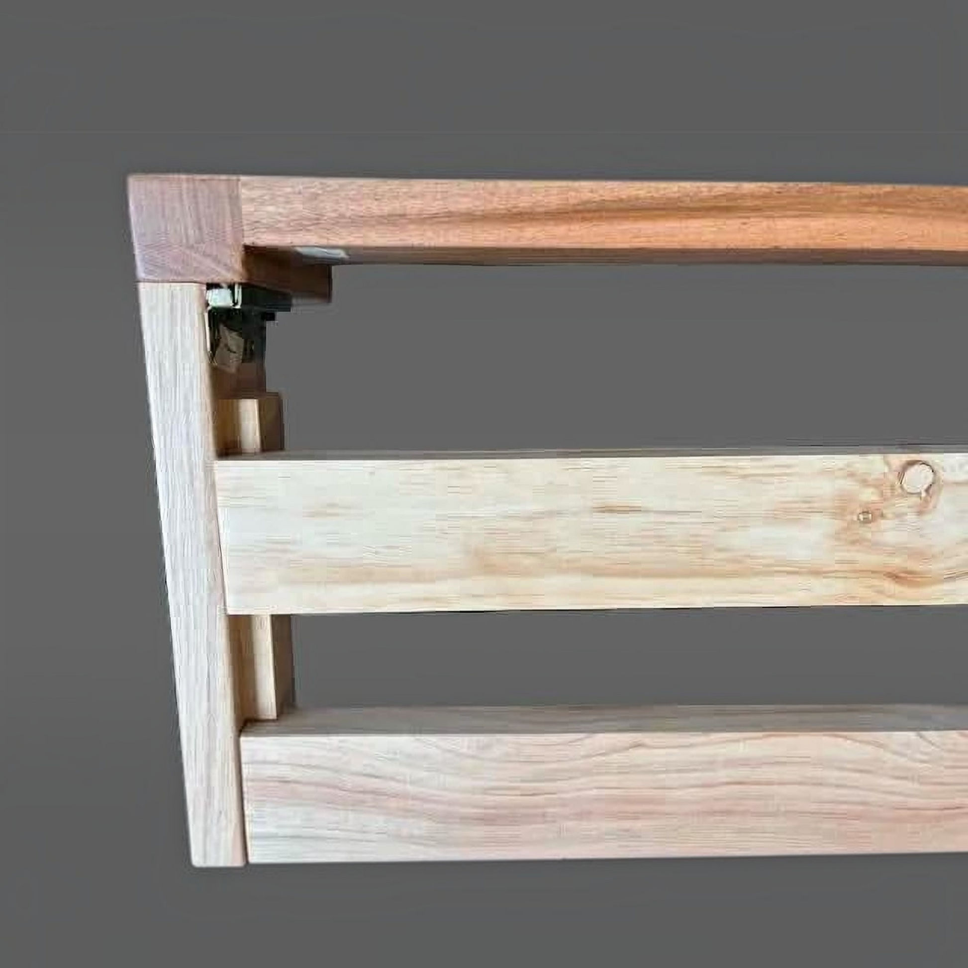 Close-up of a wooden shelf or bracket with two-tone natural wood construction, including a darker brown top rail and a lighter beige wood frame, shown against a solid gray background.
