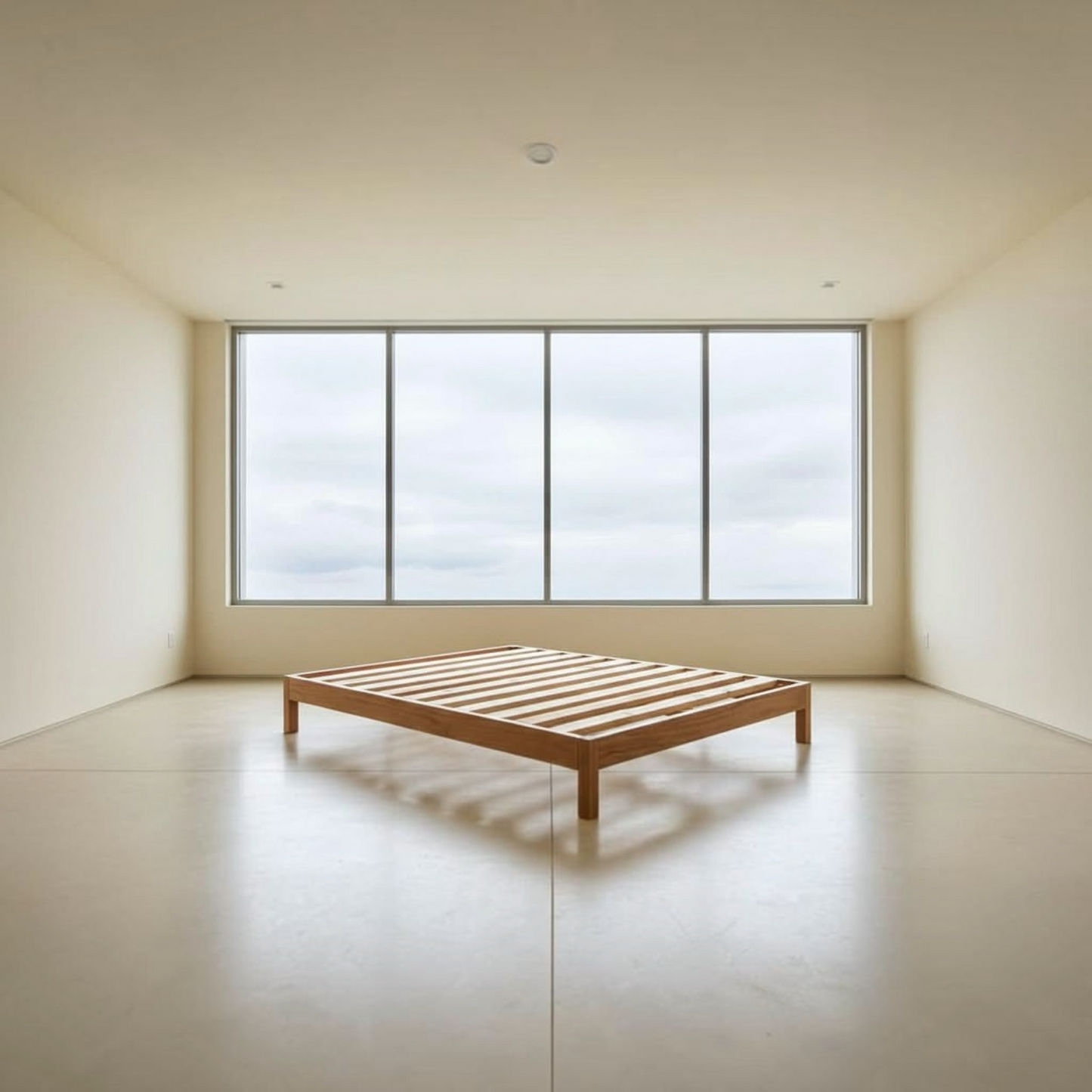 A minimalist wooden slat bed frame in a warm medium brown tone, positioned in a spacious, modern room with cream walls, a polished concrete floor, and a large multi-pane window looking out to a cloudy sky.