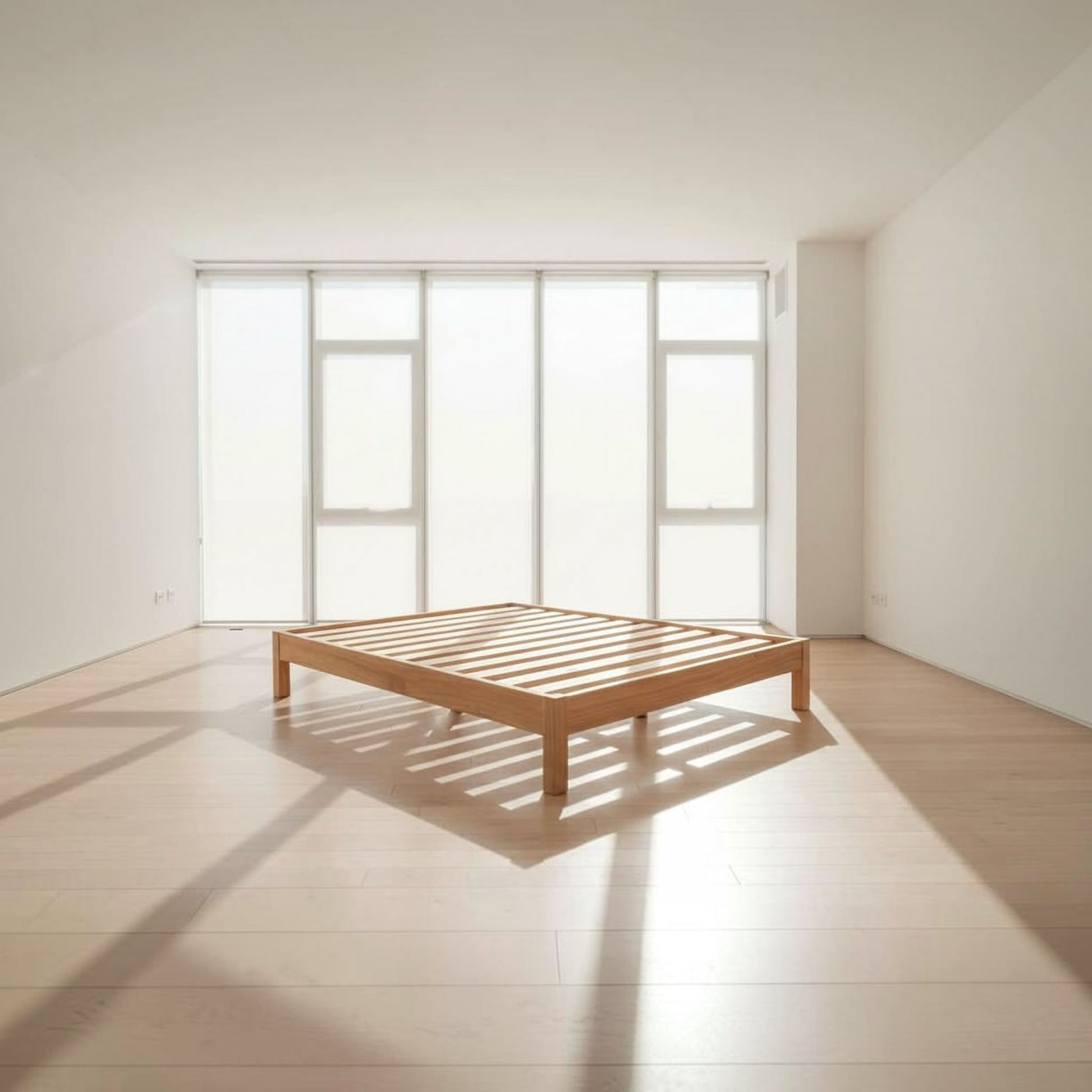 A minimalist light oak wooden slatted bed frame in a bright, modern room with white walls, large windows, and natural sunlight casting shadows on the floor.