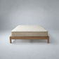 A quilted mattress on a low wooden platform bed frame, photographed against a neutral gray studio background.
