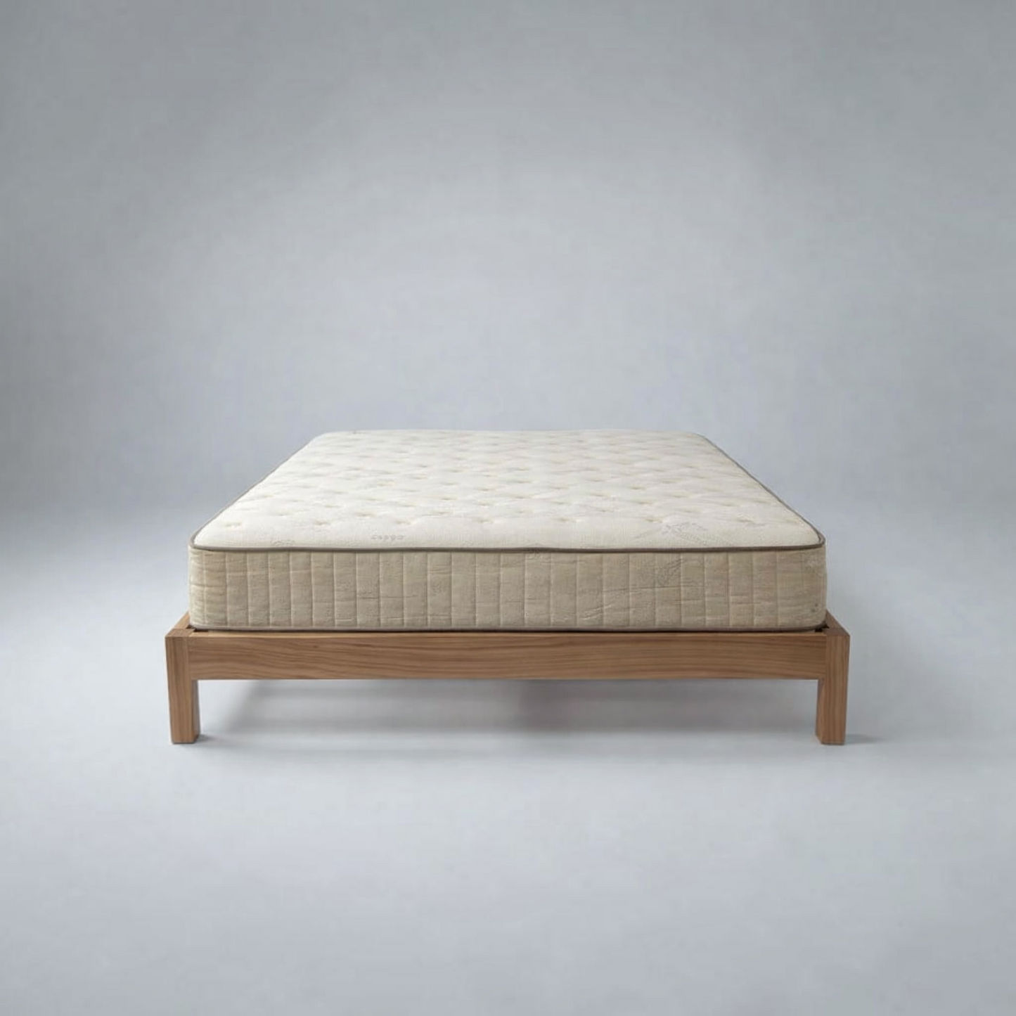 A quilted mattress on a low wooden platform bed frame, photographed against a neutral gray studio background.