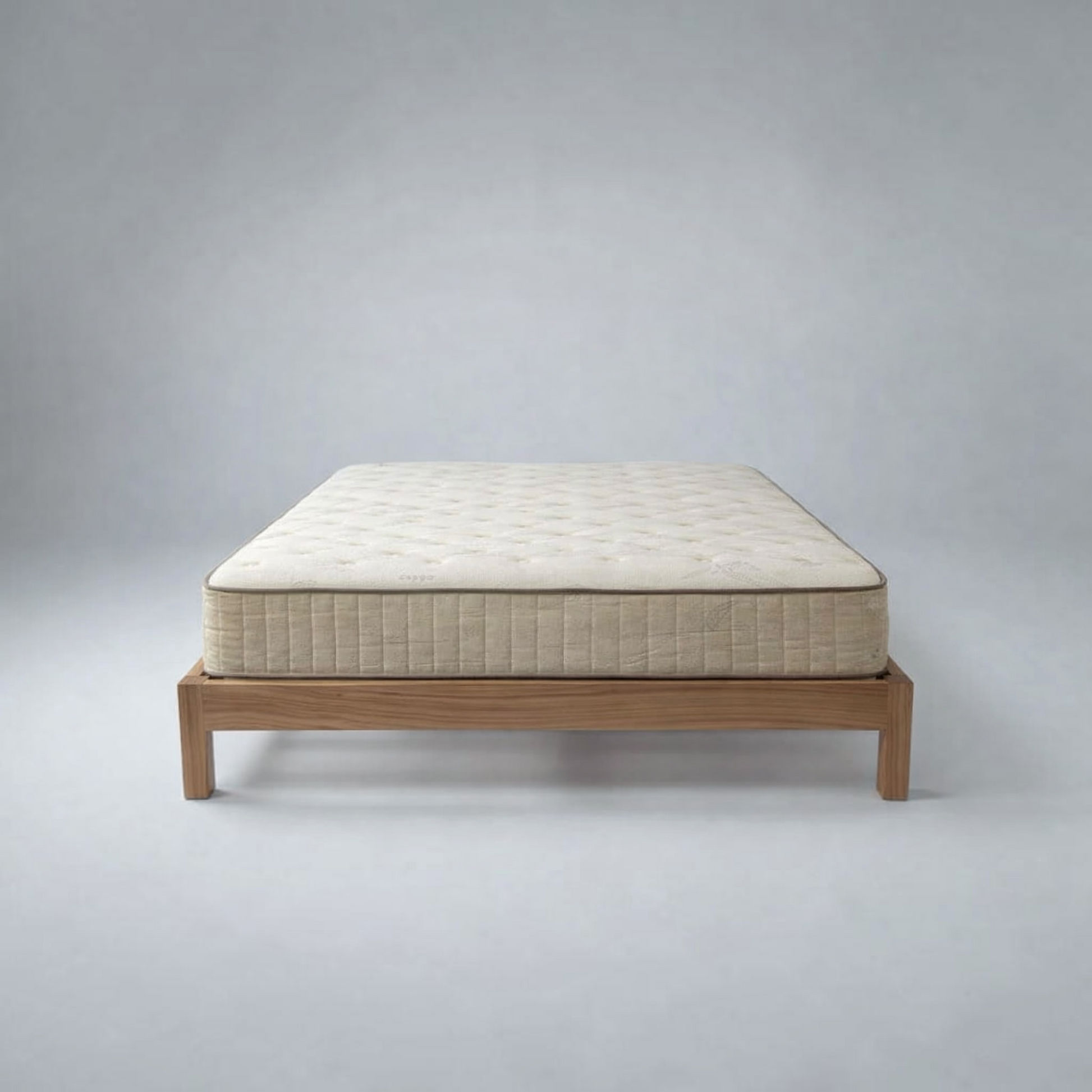 A quilted mattress on a low wooden platform bed frame, photographed against a neutral gray studio background.