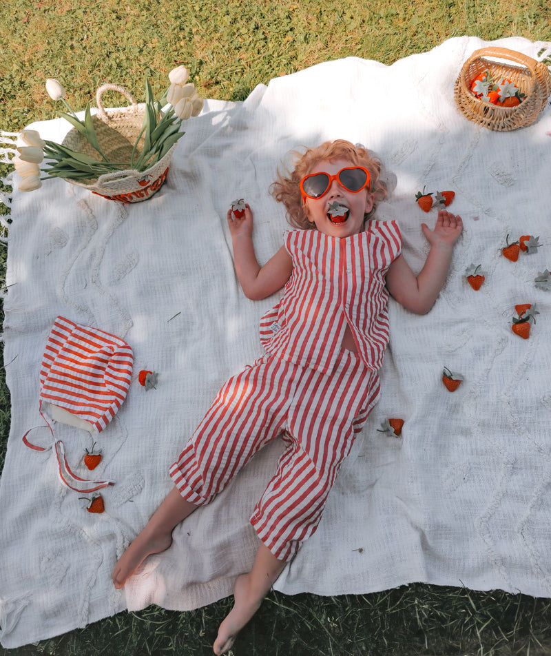 Little Girl wearing red and white coordinates lying on a picnic blanket, eating strawberries in the Summer