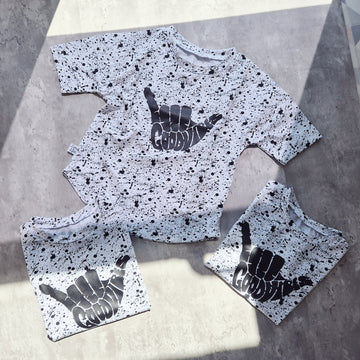 Oversized children’s T-shirt with black splatter pattern and Good Vibes Shaka print. Monochrome surf-inspired design.