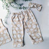 Flat lay image of a pair of kids baggy, beige trousers with white flower print. Pictured with a coordinating knotted headband. 
