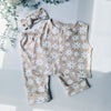 Flat lay image of a girls jersey co-ordinates set of trousers and waistcoat in beige, with white daisy style flowers