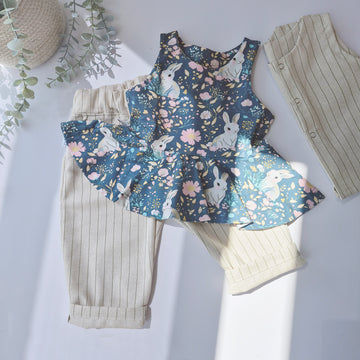A girls printed peplum vest with bunny and flower detail. Pictured alongside a pair of neutral cotton baggy trousers with pinstripe detail. Entire outfit ethically handmade in the UK, by award winning kid's brand Lottie & Lysh.