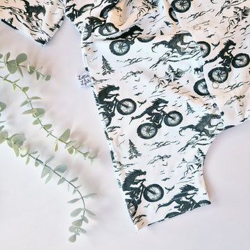 Baby onesie with dinosaur and bike pattern on a white background