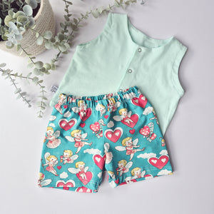 Children's outfit with a light blue sleeveless top and teal shorts with cherubs and heart pattern on a light gray background.