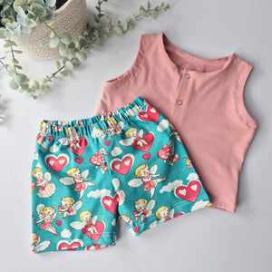 Pink sleeveless top and blue shorts with fairy and heart pattern on a light gray background