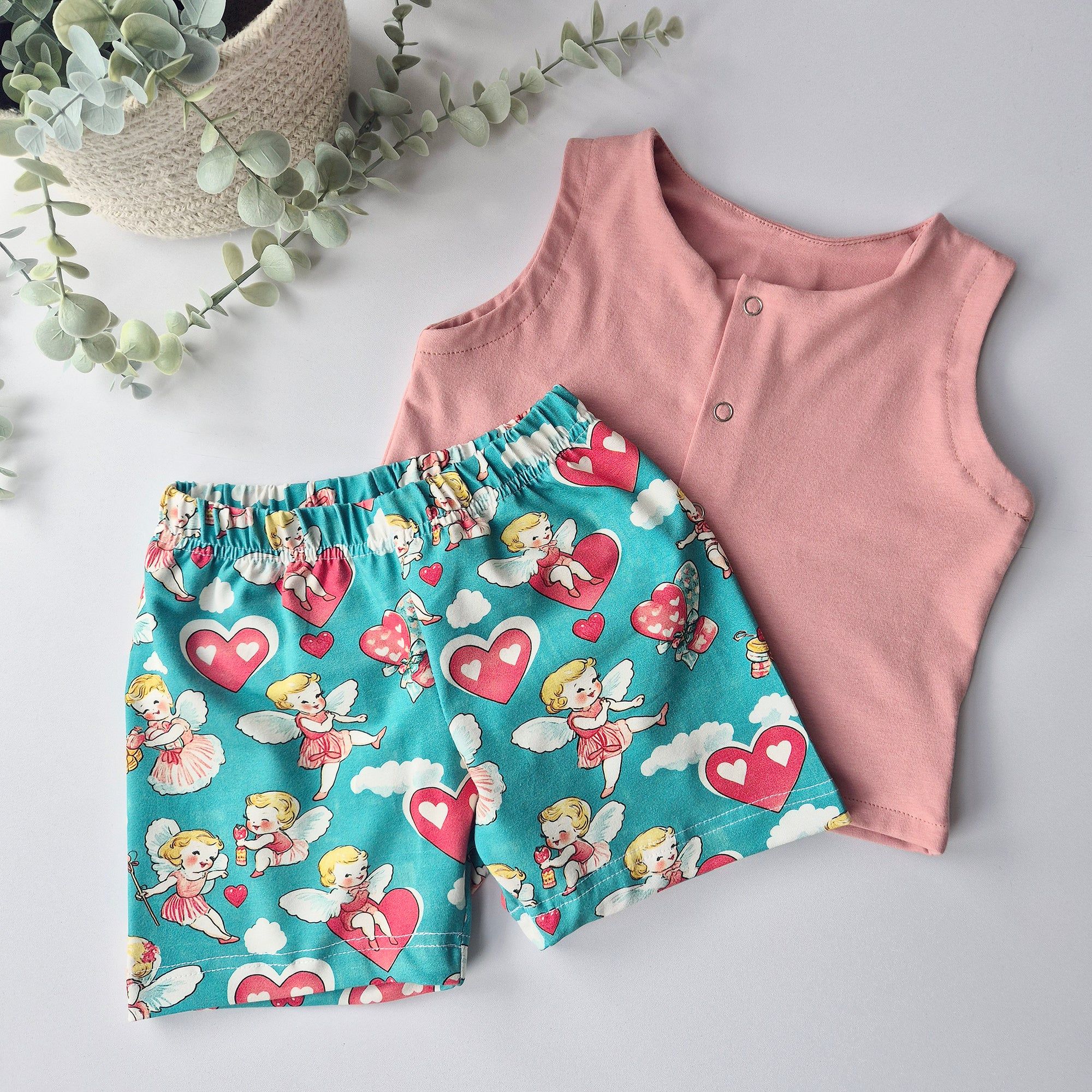 Pink sleeveless top and blue shorts with fairy and heart pattern on a light gray background