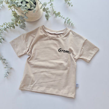 Beige t-shirt with 'Grom' text on a light background with greenery